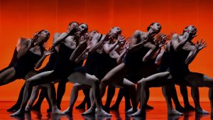 A group of Ballet BC dancers on stage in front of an orange background.