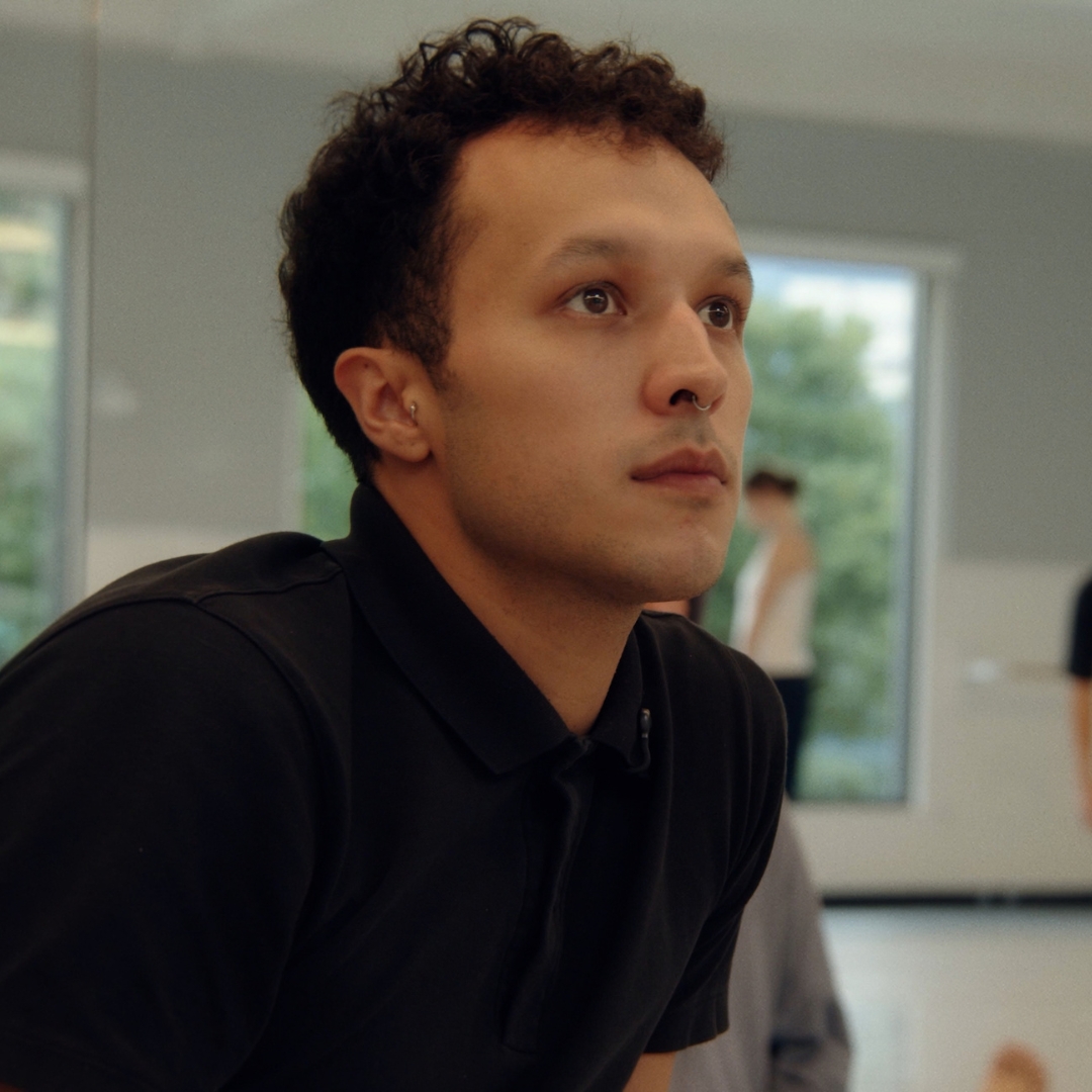 A choreographer sits at the front of a bright studio