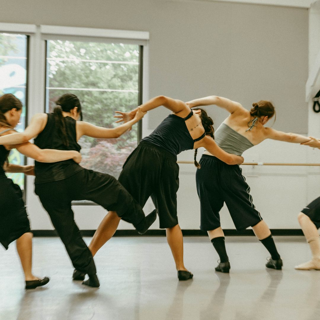 A group of dancers dressed in black rehearse in the studio