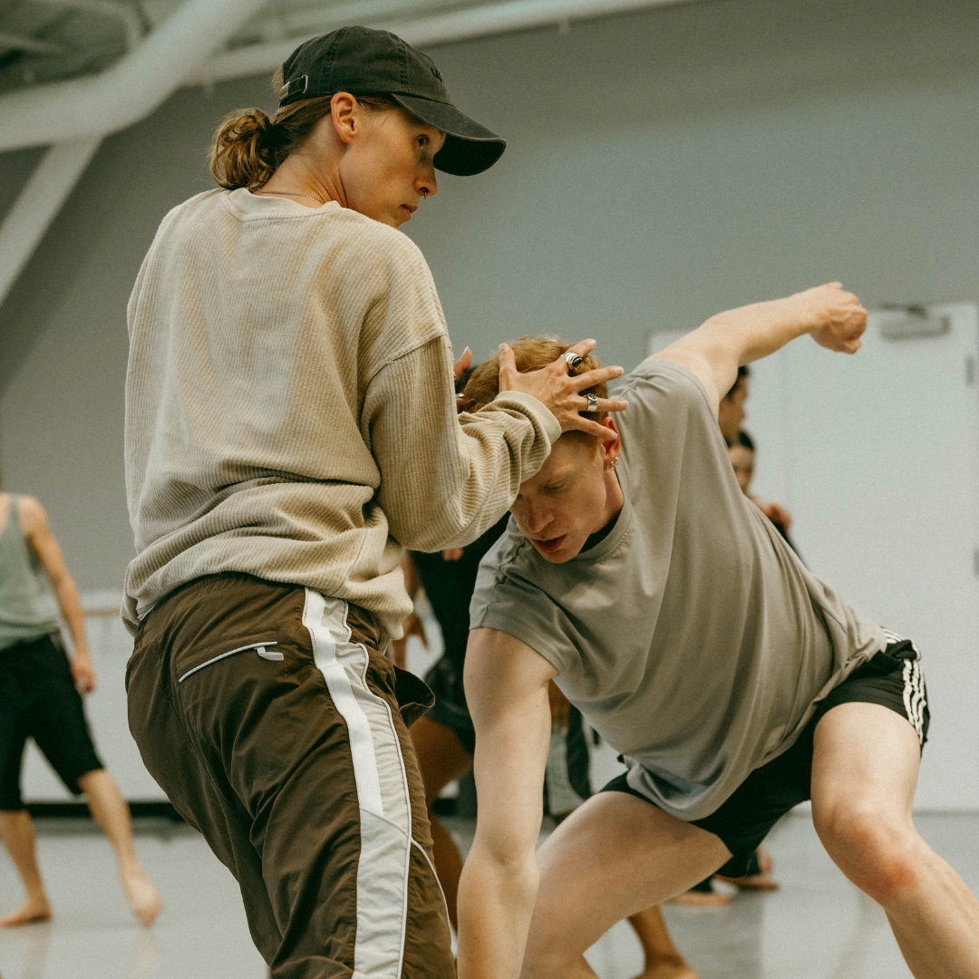 Two choreographers demonstrate for dancers in a bright studio space