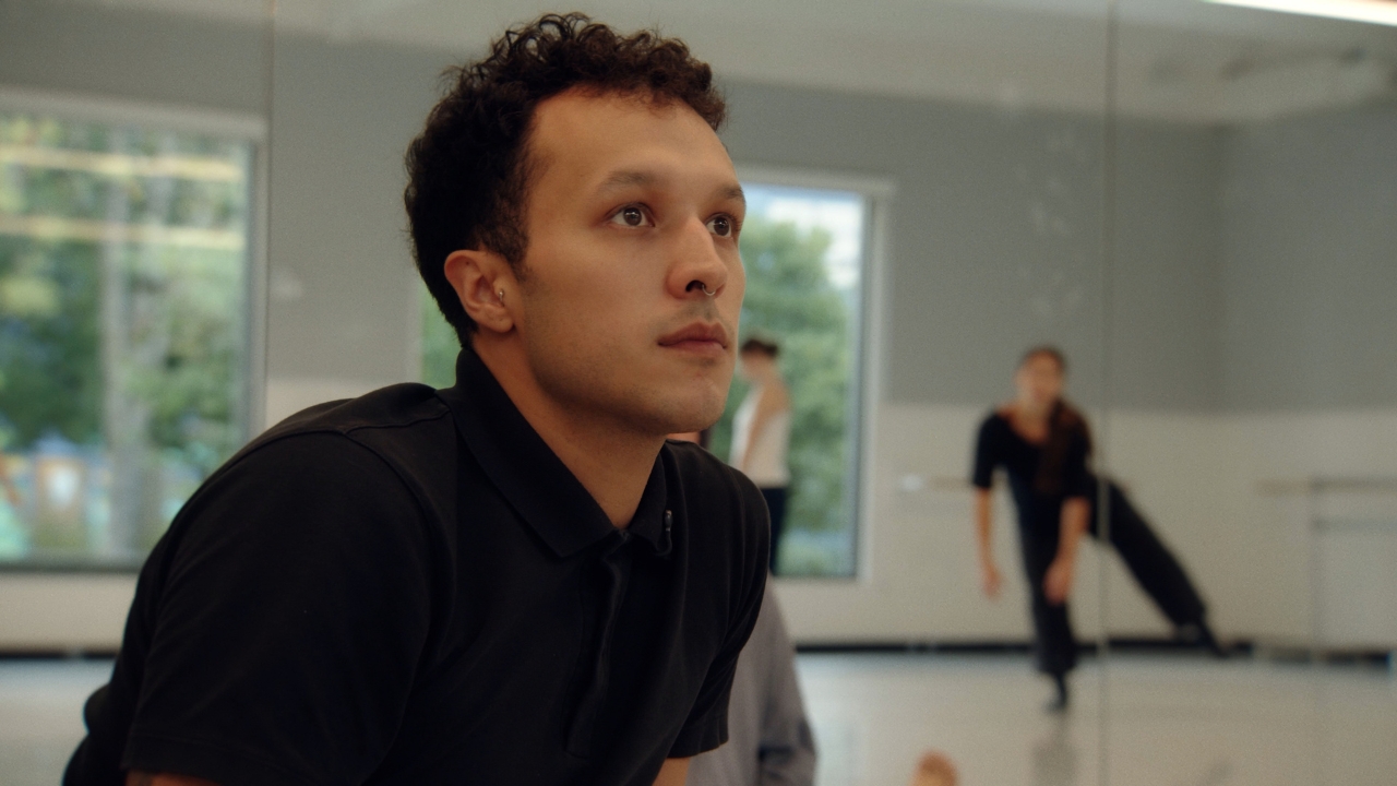 A choreographer sits at the front of a bright studio
