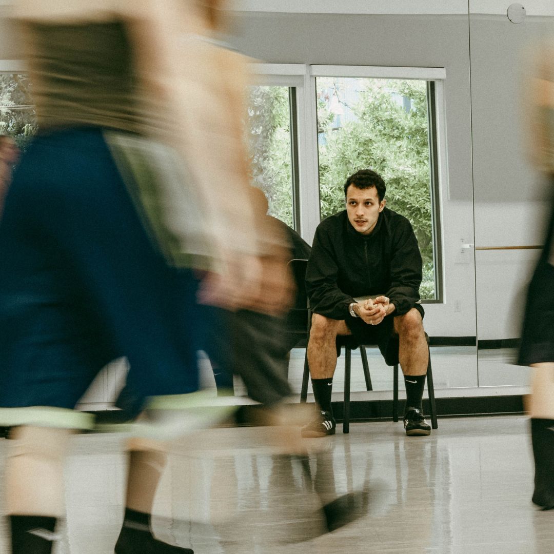 A choreographer sits at the front of a bright studio
